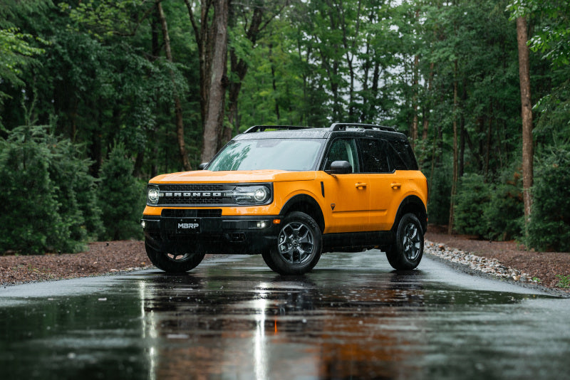 Yellow Ford Bronco on wet road amidst trees