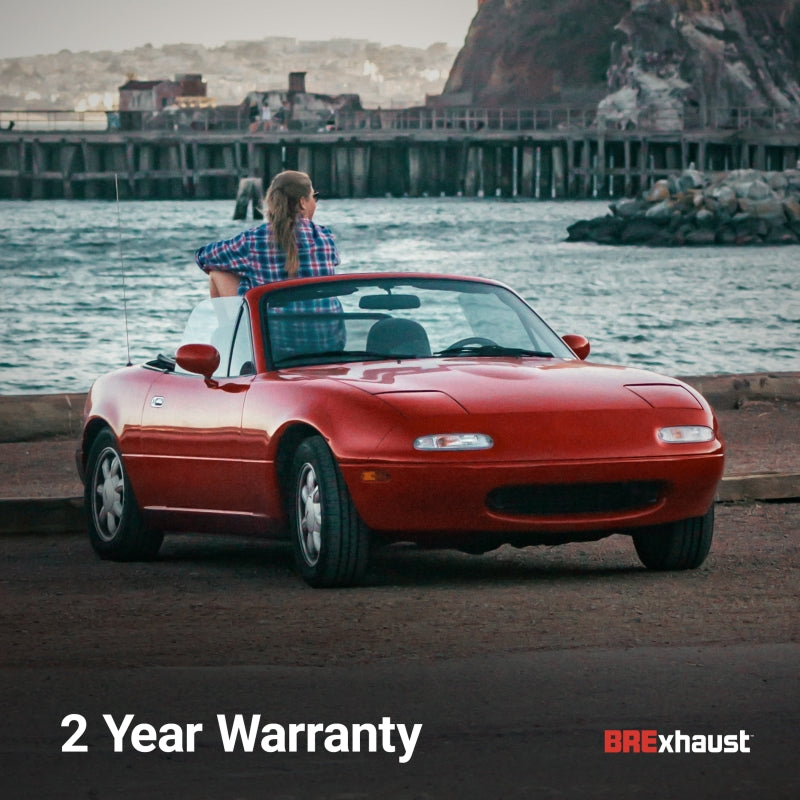 Red convertible car by ocean with BREXhaust logo and 2-year warranty text; car parked by the water with cityscape in background.