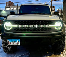 Load image into Gallery viewer, Front view of a SUV with bright headlights on in an urban setting.